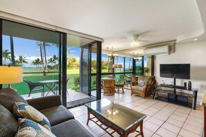 Un salon moderne avec une porte vitrée donnant sur une terrasse, un canapé, une table basse, des meubles en osier, un téléviseur à écran plat et un ventilateur de plafond.