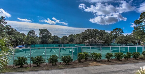 Tennis enthusiasts can enjoy a game on the outdoor court surrounded by lush greenery and trees.