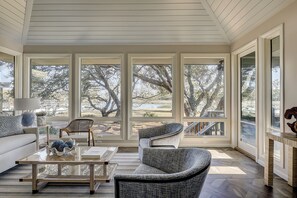 Relax in this serene sunroom with expansive views of the surrounding landscape, featuring a cozy seating area with a sofa and chairs.