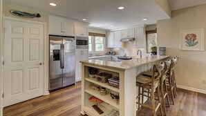 A modern kitchen with white cabinetry, stainless steel appliances, a central island with bar stools, and a wooden floor. - 6 Portside- HEATED Community Pool. Fantastic views of South Beach Marina (Hilton Head Island)
