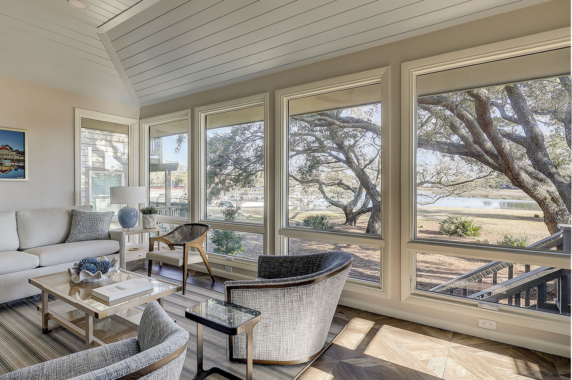 A spacious living room with a large window overlooking a scenic outdoor area, furnished with a sofa, chairs, and a coffee table.