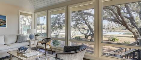 A spacious living room with a large window overlooking a scenic outdoor area, furnished with a sofa, chairs, and a coffee table.