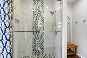 A glass-enclosed shower with a marble wall, a wooden bench, and a towel rack.