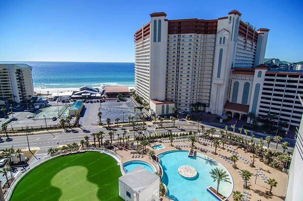 A hotel with a large pool, a golf course, and a view of the ocean.