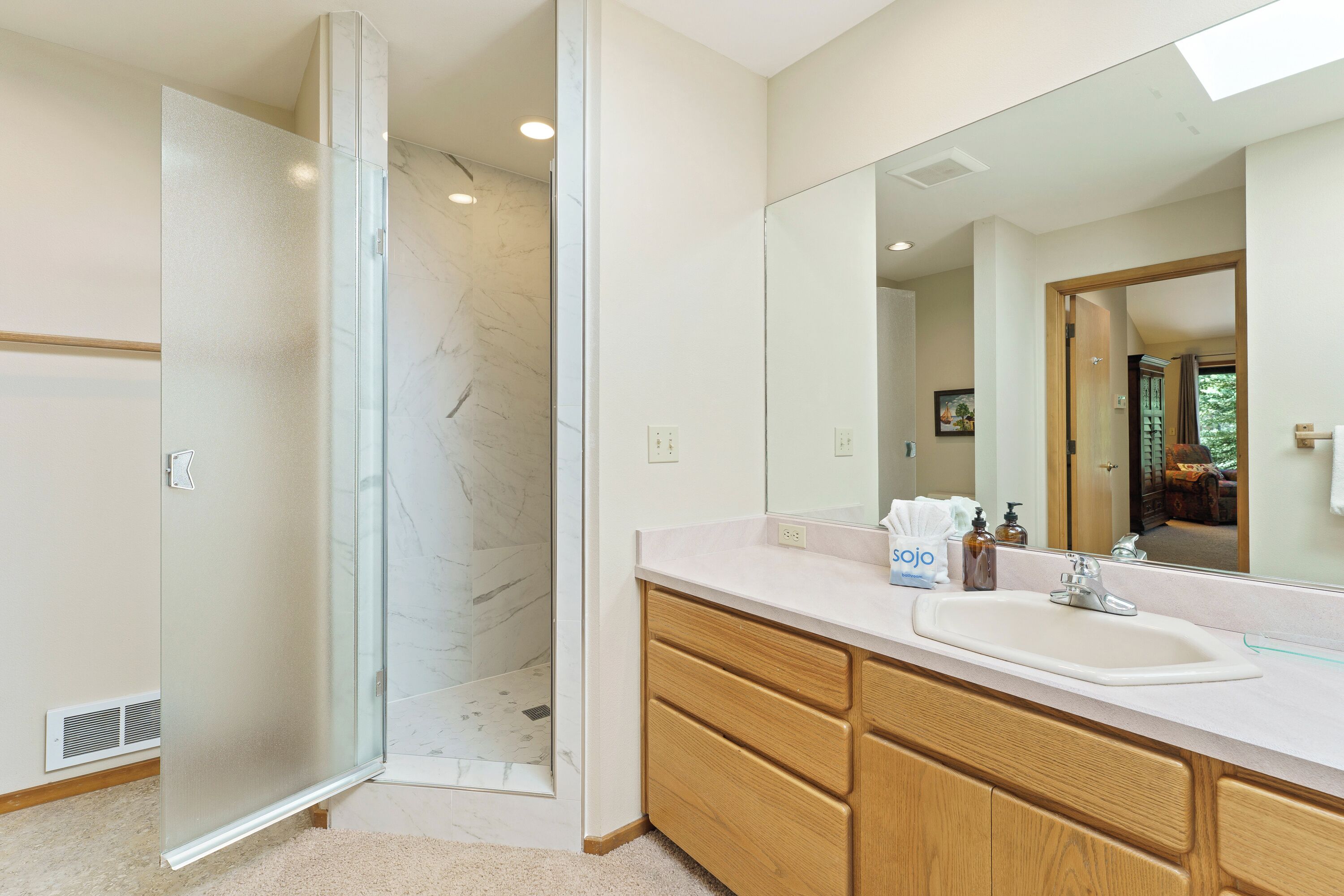 A modern bathroom with a glass shower enclosure, a large mirror, and wooden cabinetry.