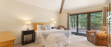 A bedroom with a large bed, bedside tables, a chair, and a view of trees through large windows.
