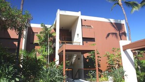Ein modernes Gebäude mit Balkon, umgeben von Palmen und Grünpflanzen.