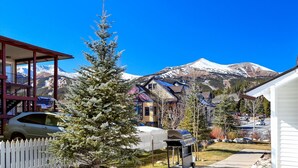 Un barrio residencial con una montaña nevada al fondo, casas con tejados de colores y una cerca blanca de piquetes.