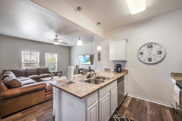 A modern kitchen with a granite countertop, white cabinetry, and a built-in island with a sink.
