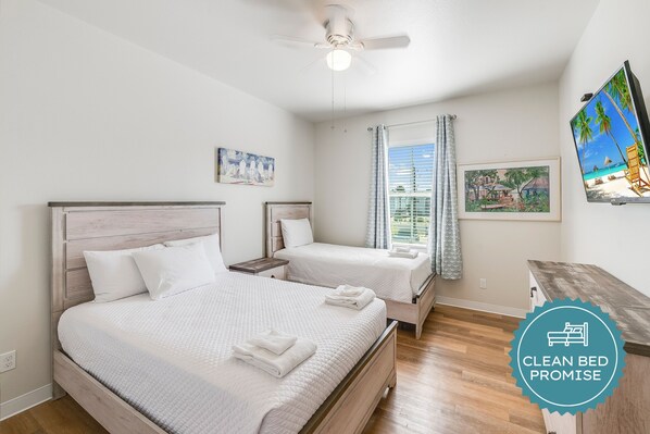 A clean, well-lit bedroom with two beds, a ceiling fan, and artwork on the walls.