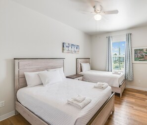 A clean, well-lit bedroom with two beds, a ceiling fan, and artwork on the walls. - Short Walk to Beach | Heated Pool & Family Comfort (Corpus Christi)