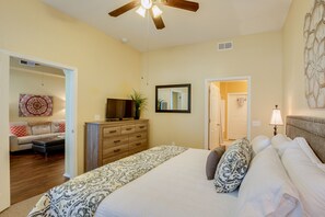 A bedroom with a bed, dresser, TV, and a ceiling fan.
