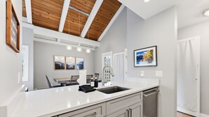 Una cocina moderna con encimera blanca, armarios grises, pileta de acero inoxidable e iluminación colgante.