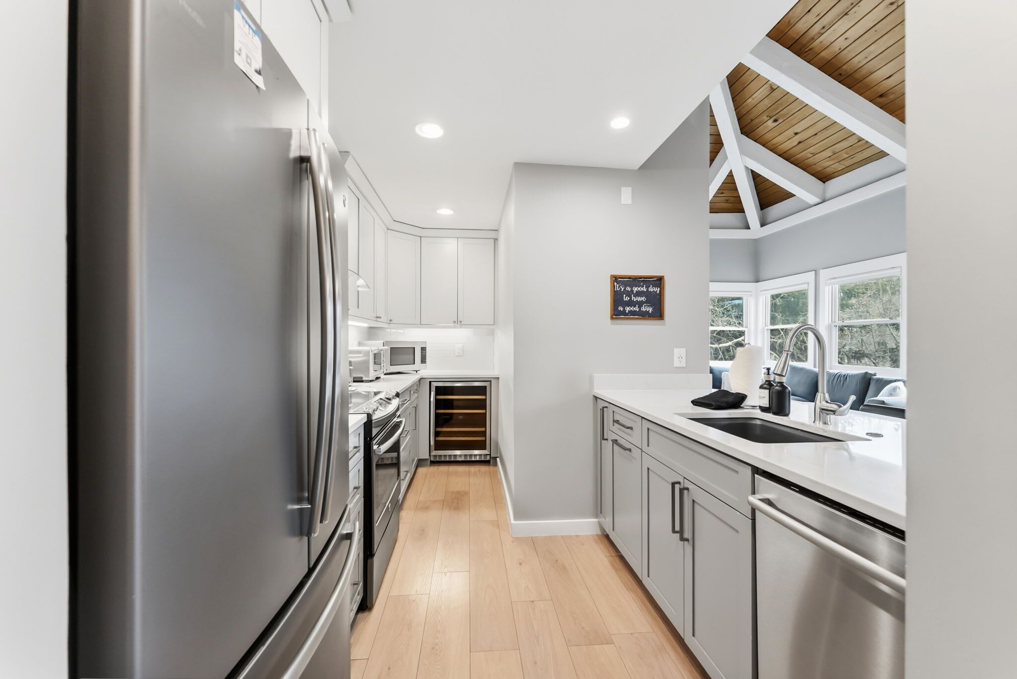 A modern kitchen with stainless steel appliances, a built-in oven, microwave, and a dishwasher. There is a window with a view of greenery outside.