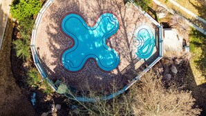 Ein Luftbild eines Schwimmbeckens mit einem einzigartigen Wellenmuster, umgeben von einer Ziegelterrasse und Grünflächen.