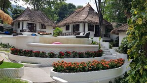 A resort with thatched-roof cottages, white outdoor seating, and tiered flower beds. - Clear View Resort (Koh Tao)