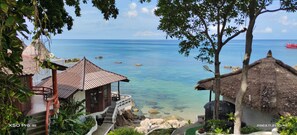 A coastal view with a thatched-roof structure, a small building with a balcony, and a clear blue sea.