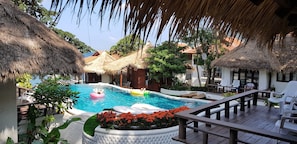A pool area with a thatched-roof structure, lounge chairs, and a wooden deck.