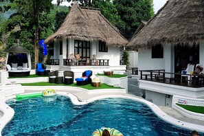 A pool area with lounge chairs, a thatched-roof building, and a small inflatable pool.