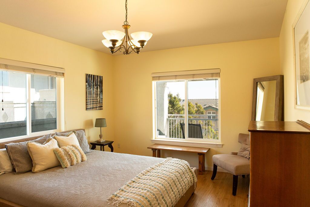 A bedroom with a large bed, a chandelier, a bench, and a view of the outside.