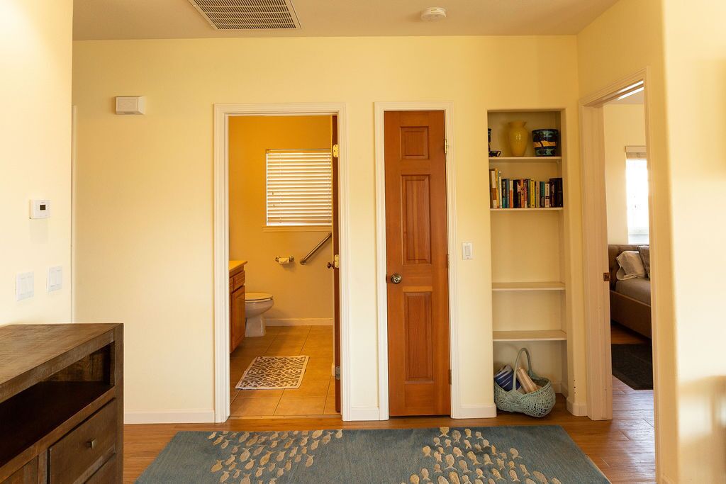 Un pasillo con suelo de madera, un tapete, una estantería y una puerta que da a un baño.