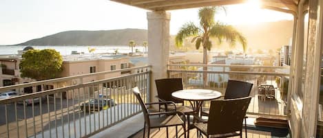 A balcony with a table and chairs, overlooking a street and a body of water.