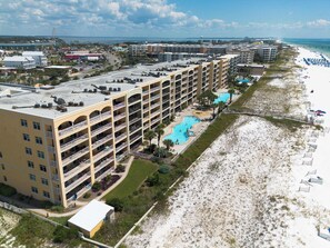 A multi-story hotel with a rooftop pool, adjacent to a beach with sun loungers and umbrellas.
