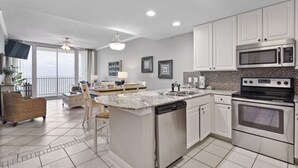 A modern kitchen with white cabinets, a granite countertop, a dishwasher, a microwave, and an oven. - Lighthouse 1413 by Liquid Life (Gulf Shores)