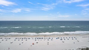 A beach with rows of umbrellas and beach chairs, a sandy shore, and the ocean. - Lighthouse 1413 by Liquid Life (Gulf Shores)