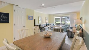 A dining area with a wooden table, chairs, and a bowl. There is a sofa and a chair in the background.