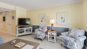 A living room with a TV, two patterned armchairs, a coffee table, and a side table with a lamp.