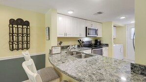A kitchen with white cabinets, a granite countertop, a microwave, a coffee maker, and a sink.