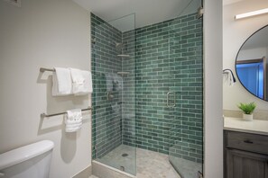 Un baño moderno con ducha envuelta en vidrio, azulejos blancos y un espejo redondo.