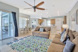 Un vaste espace de vie agrémenté d’un ventilateur de plafond, d’un tapis à motifs et d’un canapé avec des coussins.