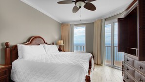 Un dormitorio con una cama grande, un ventilador de techo, un aparador y vistas al océano desde la ventana.