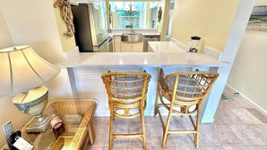 A compact kitchen with a central island, two wicker chairs, a small table, and a lamp. - Wonderful Lake View! Golf Cart Included 5080BW (Miramar Beach)