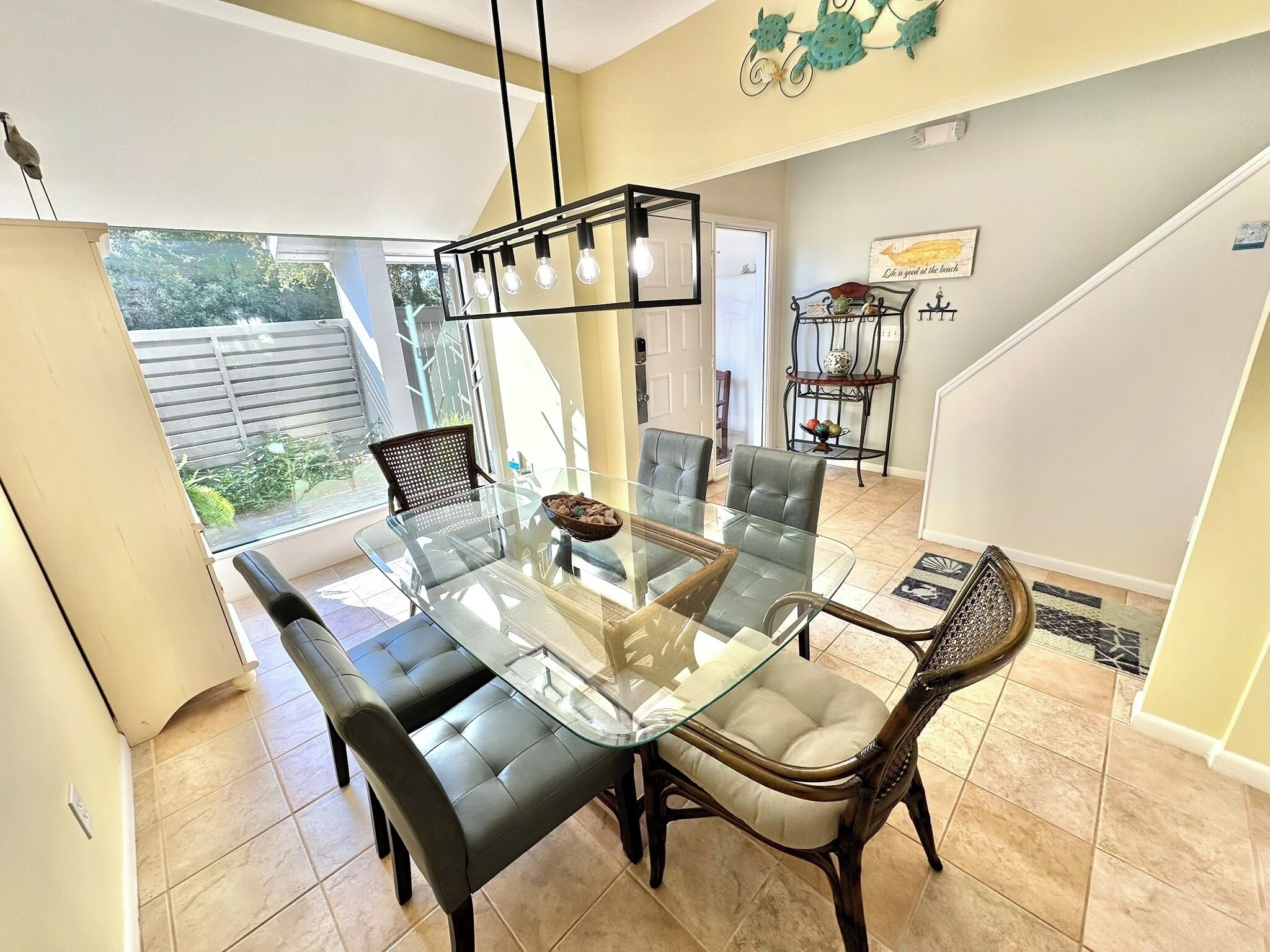 A dining area with a glass-top table, cushioned chairs, a chandelier, and a view of the outdoors.