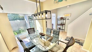 A dining area with a glass-top table, cushioned chairs, a chandelier, and a view of the outdoors. - Wonderful Lake View! Golf Cart Included 5080BW (Miramar Beach)