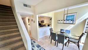 A dining area with a glass table and chairs, a kitchen in the background, and a staircase leading to another level. - Wonderful Lake View! Golf Cart Included 5080BW (Miramar Beach)