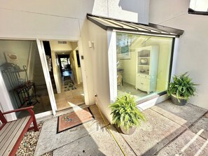 A modern house with a glass door entrance, a visible kitchen area, and two potted plants on the porch.