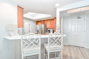 A modern kitchen with a central island, white bar stools, and a skylight.
