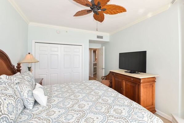 Un dormitorio con cama, televisión, aparador de madera y ventilador de techo.