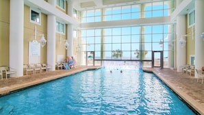 Une piscine intérieure avec des parois en verre transparent, un sol carrelé et plusieurs chaises longues disposées autour de la piscine.