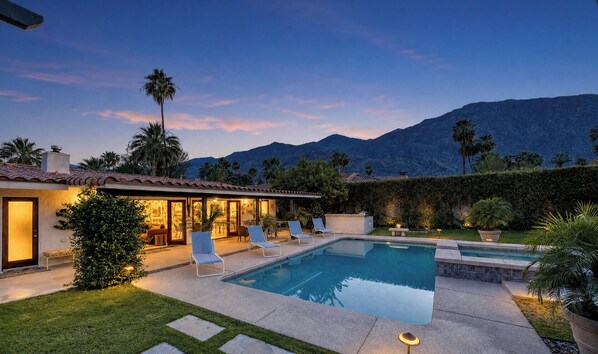 A poolside area with lounge chairs, a swimming pool, and a mountain backdrop.