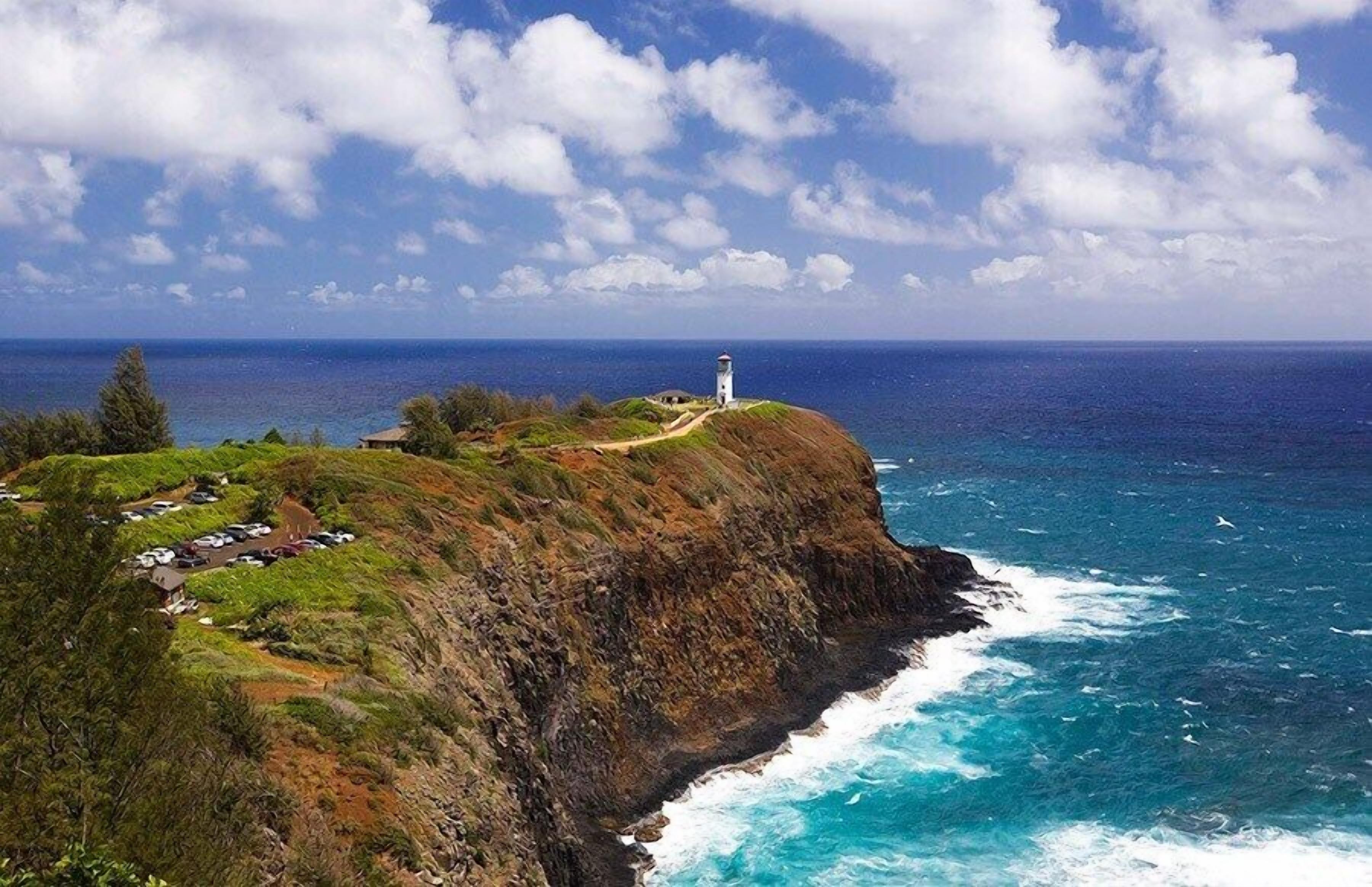 Un paisaje costero con un faro en un acantilado, un área de estacionamiento y vistas al océano.