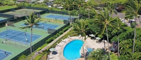 A tennis court complex with multiple courts, a swimming pool, and surrounding palm trees.