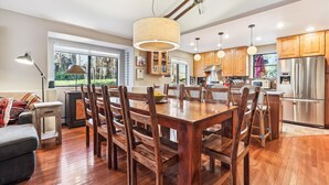 Een moderne keuken met houten kastjes, een koelkast van roestvrij staal en een eethoek met een houten tafel en stoelen.
