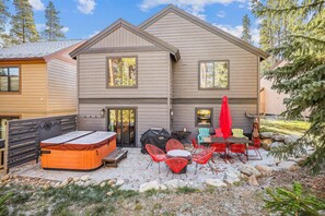 Una casa de dos pisos con un porche cubierto, mobiliario exterior y un jacuzzi.