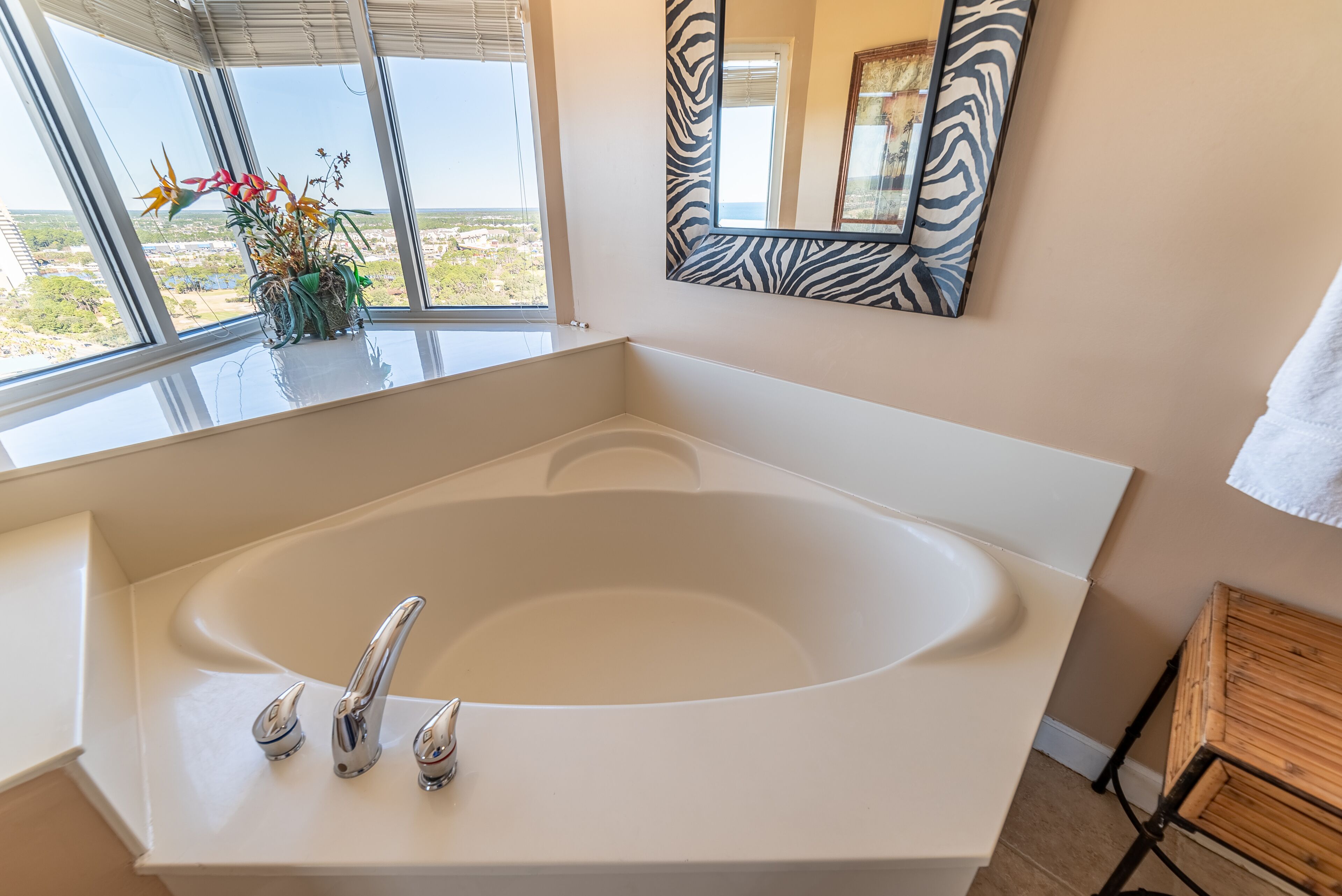 Une salle de bain moderne dotée d’une grande baignoire, d’un miroir à motifs zébrés et offrant une vue sur le paysage grâce à de grandes fenêtres.