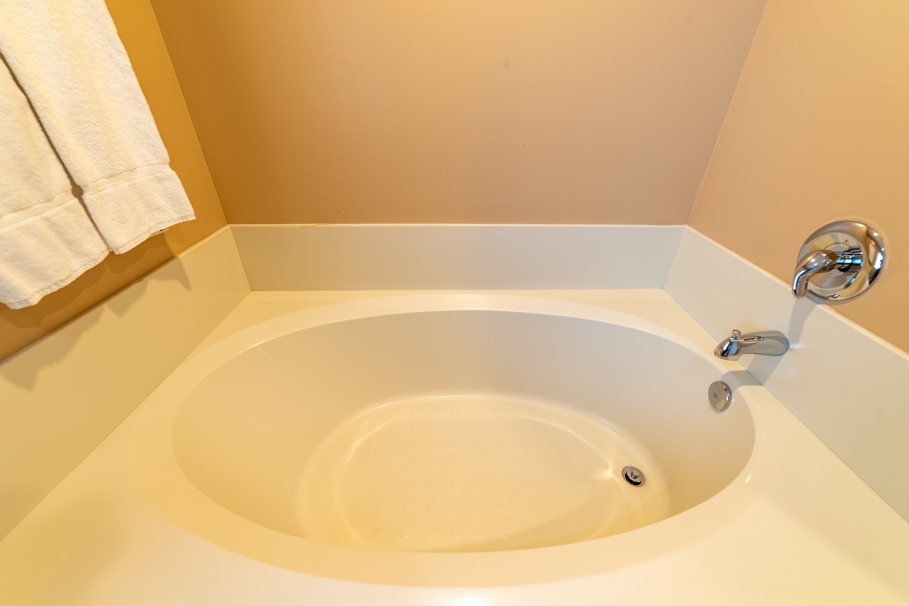A white bathtub with a chrome faucet in a bathroom with beige walls.